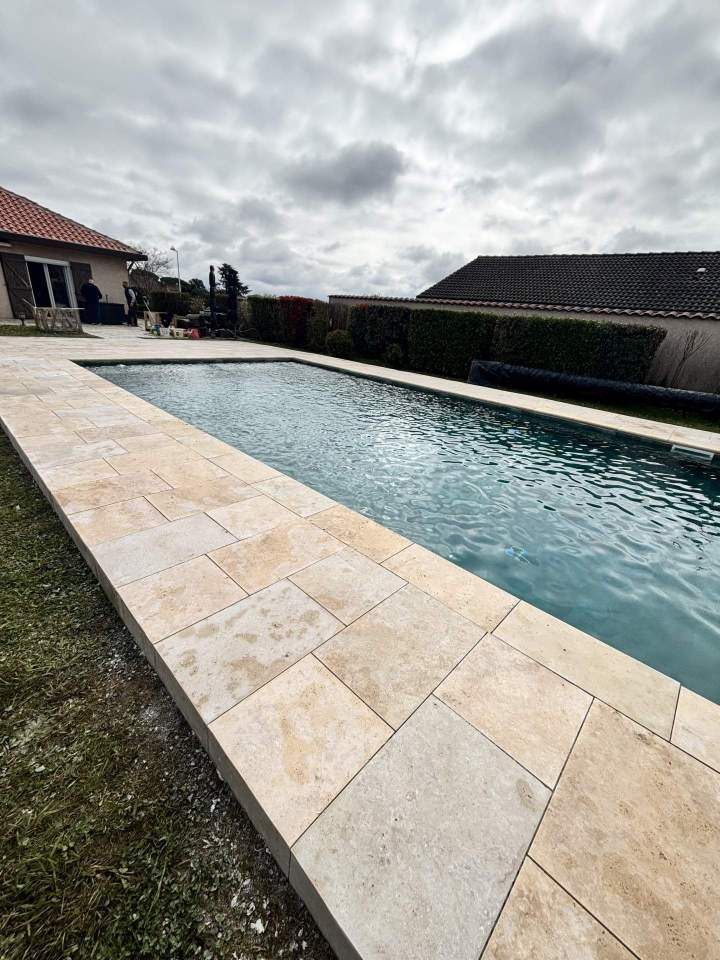 Pose de travertin naturel autour de piscine avec finitons soignées.